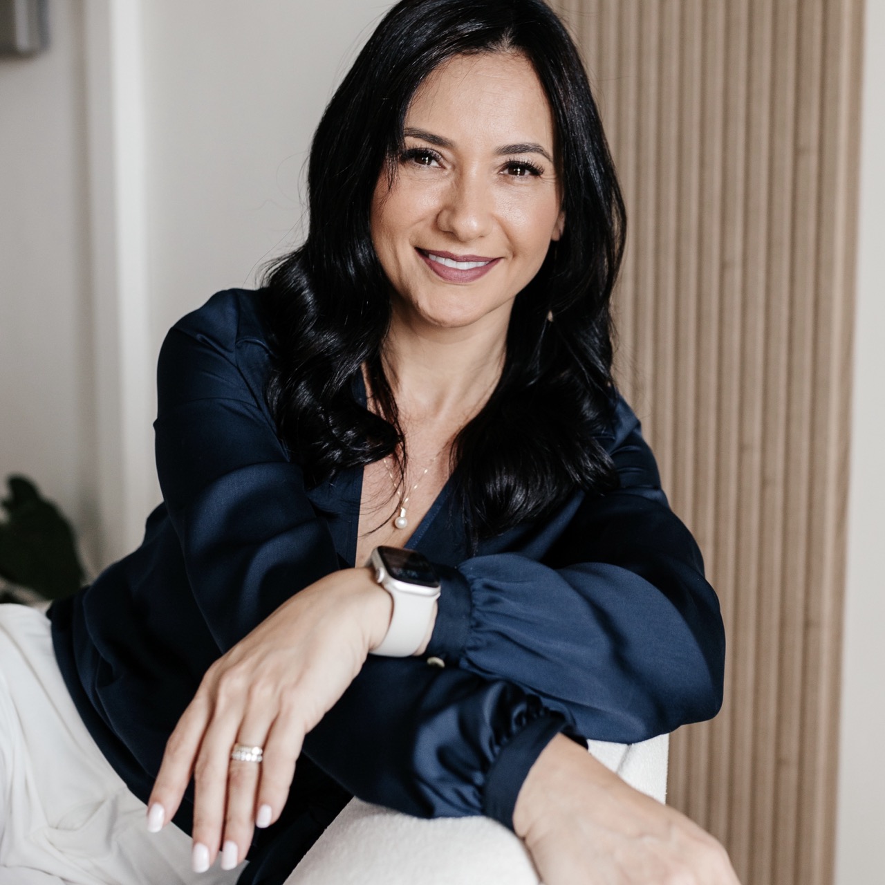 Retrato de Lilian Sanada sorrindo, de blusa azul marinho, sentada em poltrona clara